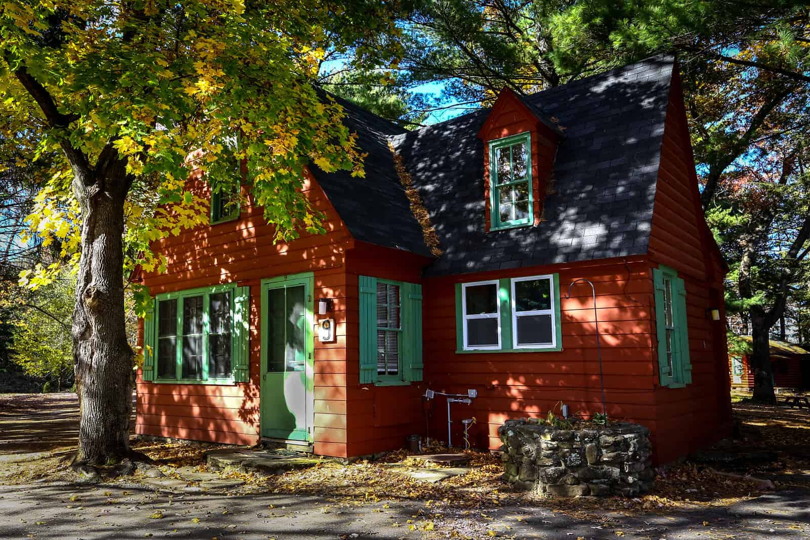 Vibrant, red storybook-style cabin with bright green trim surrounded by trees.