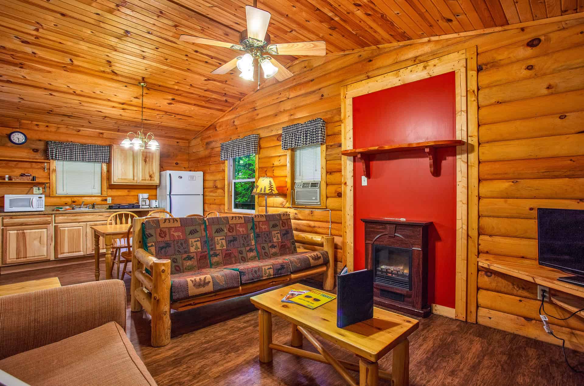 A charming log cabin interior featuring a full kitchen, a cozy living area with a patterned sofa, and a decorative fireplace.