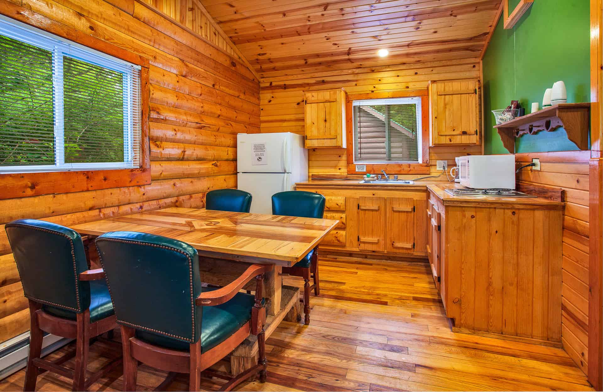 A charming cabin kitchen and dining area with warm wood-paneled walls, a wooden table with dark chairs, a refrigerator, and a microwave.