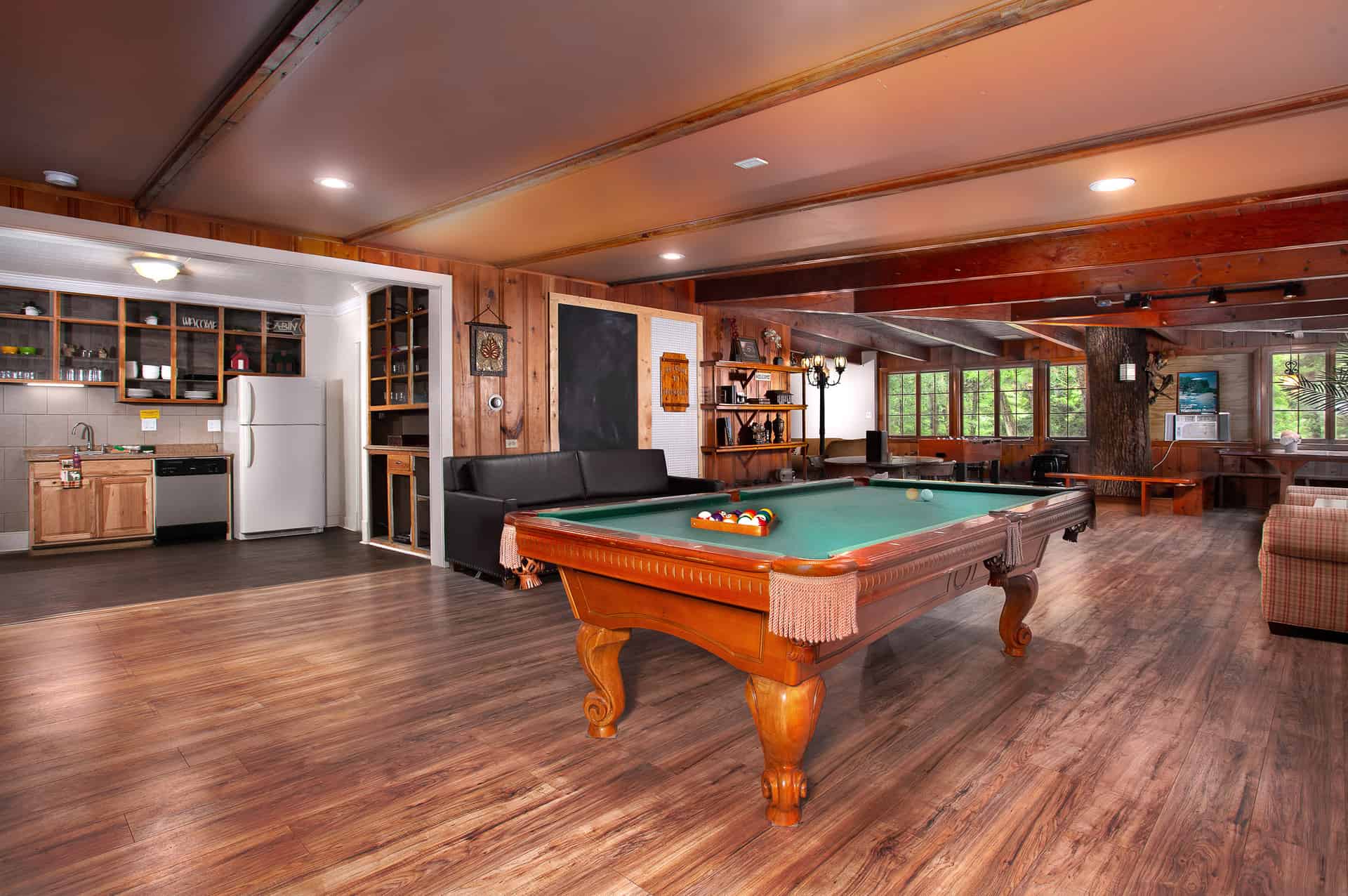 A spacious recreational area featuring a pool table, a comfortable seating area, a kitchen, and warm wooden floors and ceilings.