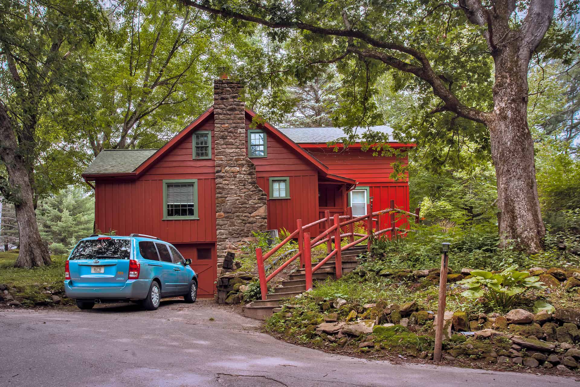 A charming red house with a prominent stone chimney and a bright red staircase, nestled among lush green trees.
