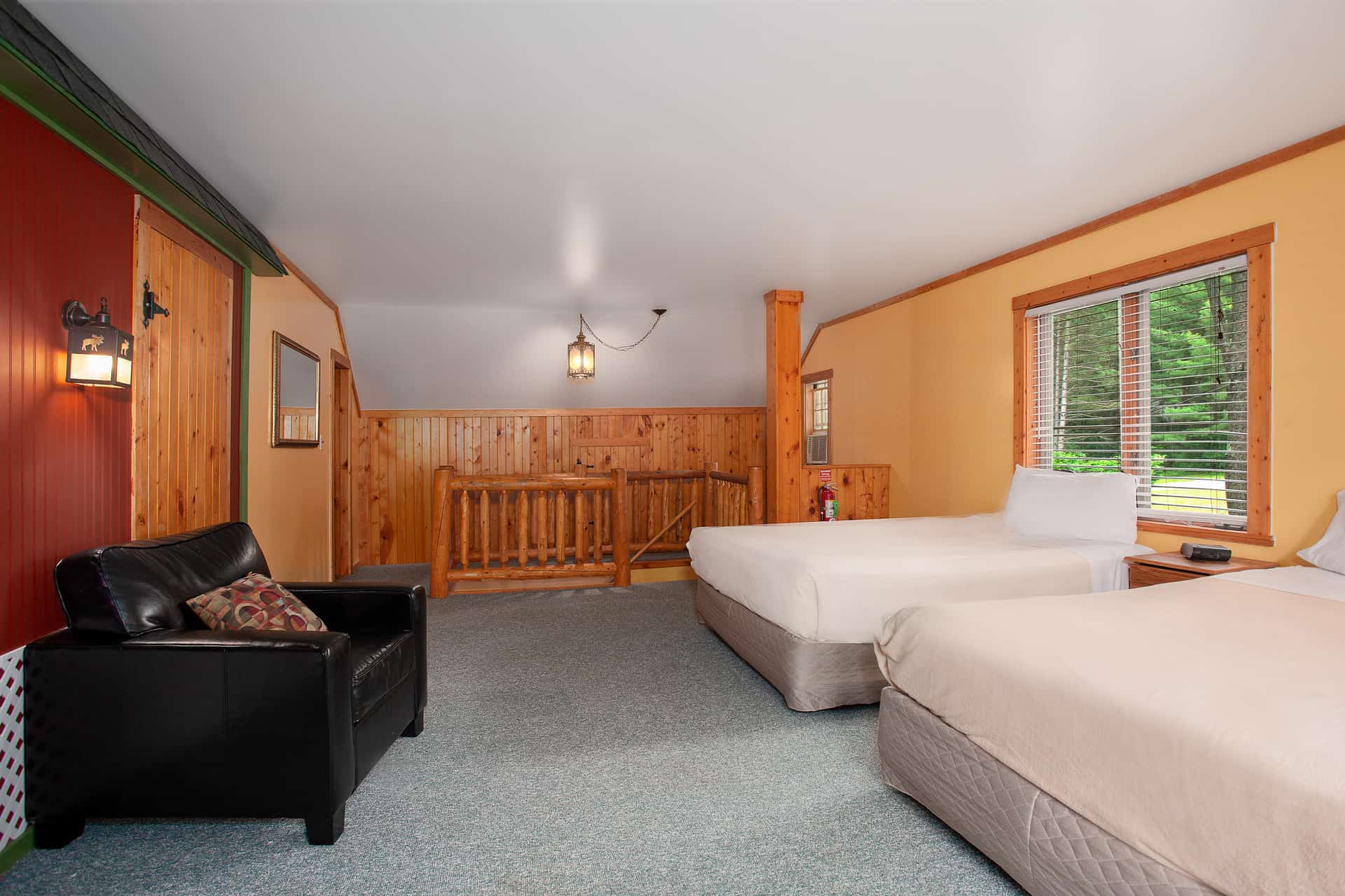 A multi-level room with a blue carpet, featuring two beds on the main level, a black armchair, and a wooden railing leading to an upper landing.