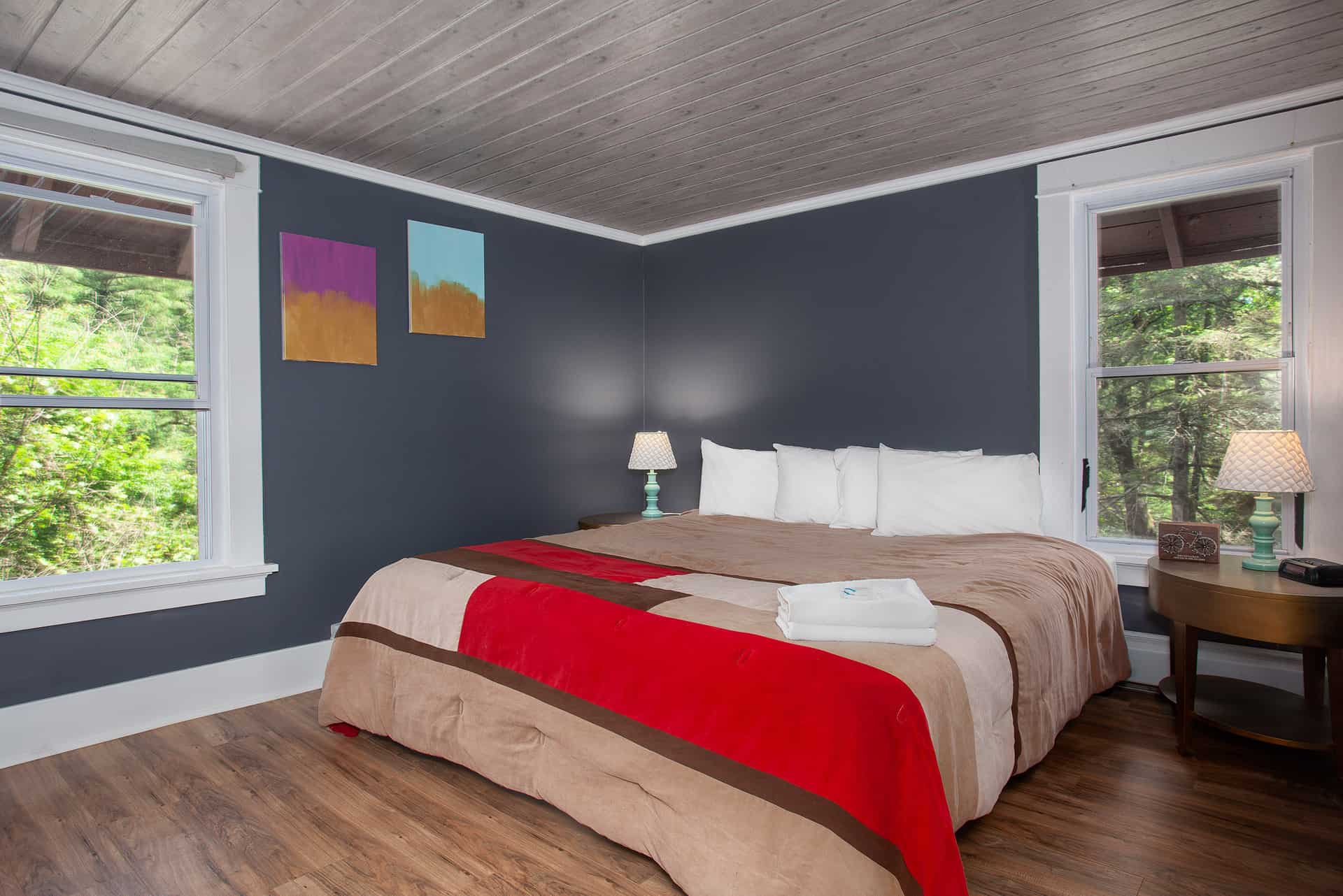 Cozy bedroom with a dark blue wall, a king-size bed, and large windows overlooking greenery.