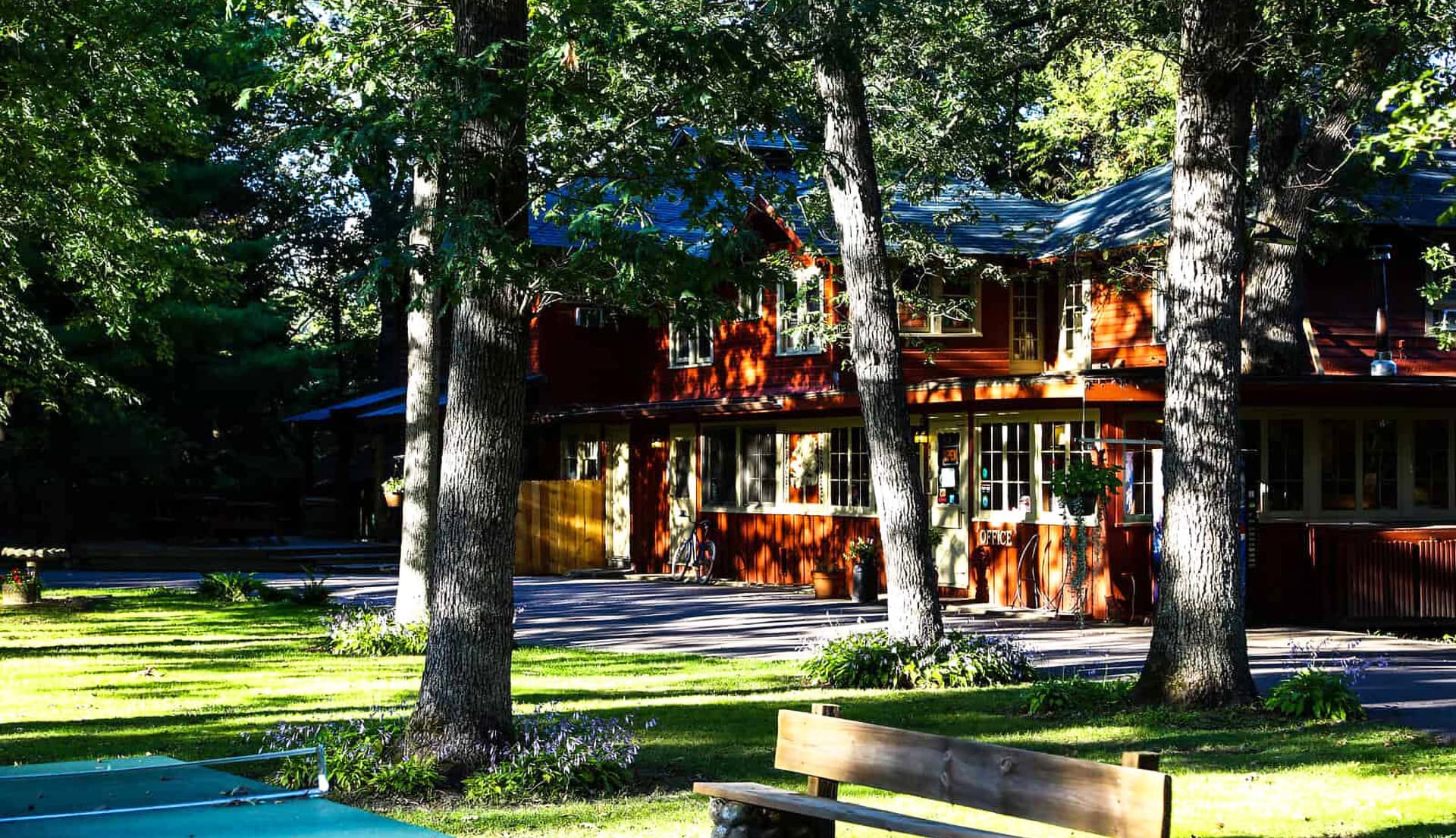 A red wooden house surrounded by trees and a grassy area.