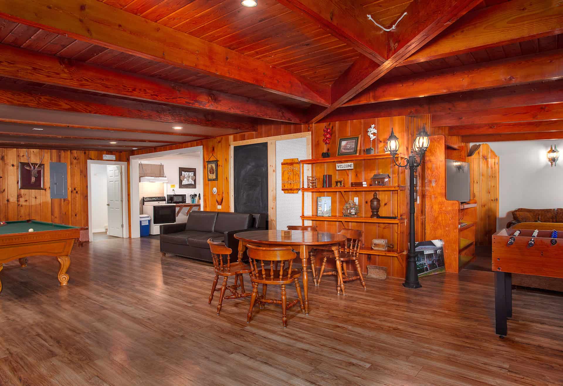 A spacious lodge recreation area with wood-paneled walls and ceiling, featuring a dining table, seating areas, a foosball table, and a pool table.