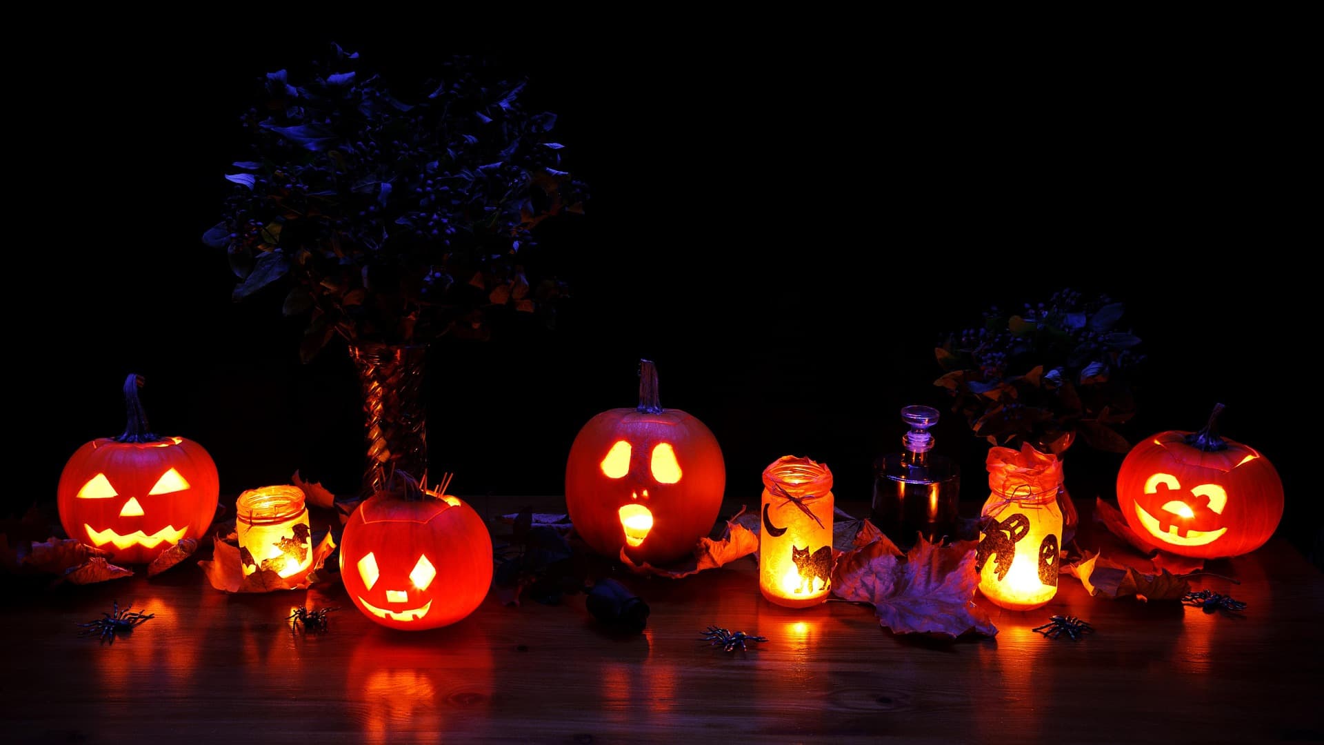 A row of illuminated carved pumpkins and spooky candles against a dark background, creating a festive Halloween atmosphere.