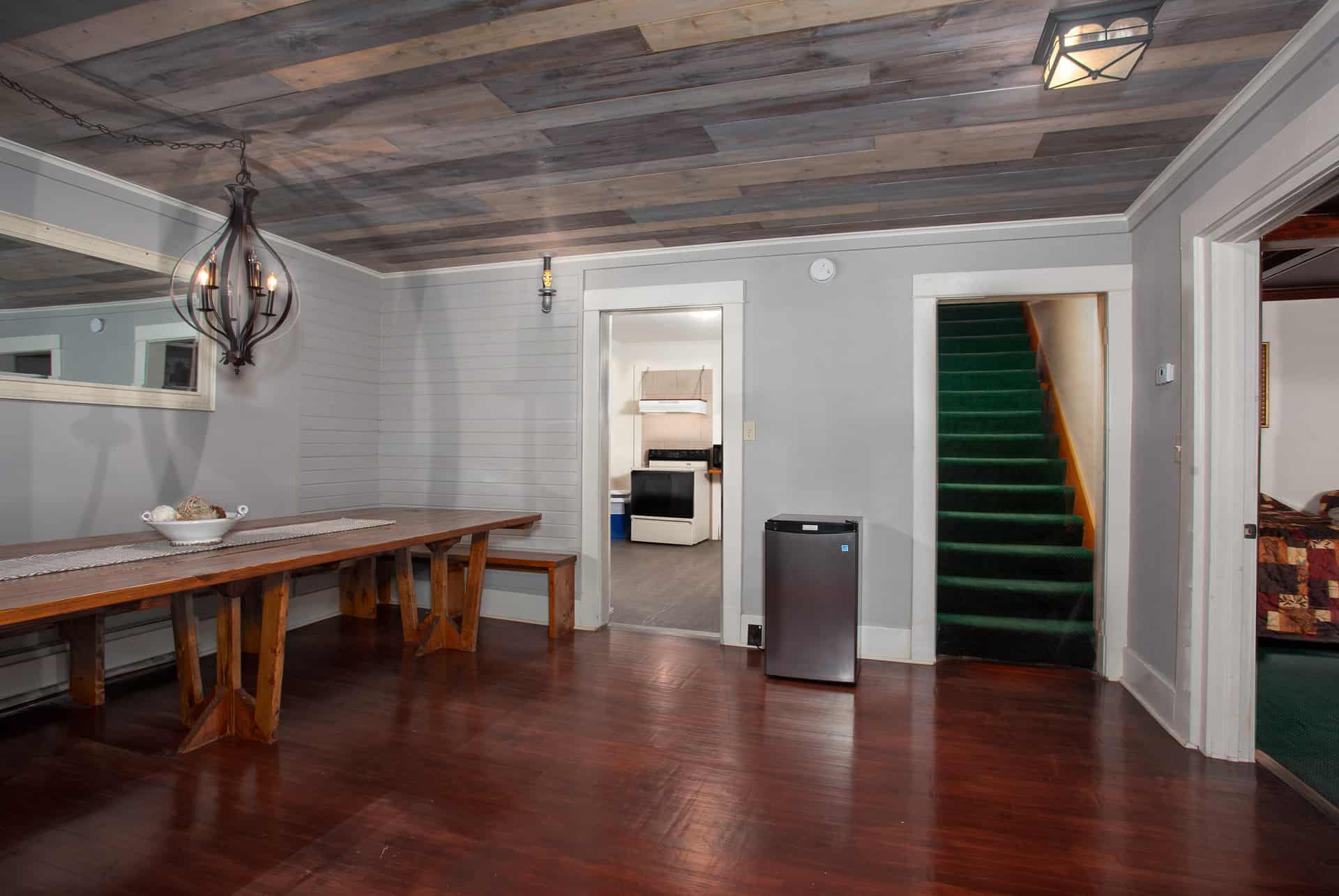 A dining area with a wooden table, a fridge, and a view of a staircase leading to an upper level.