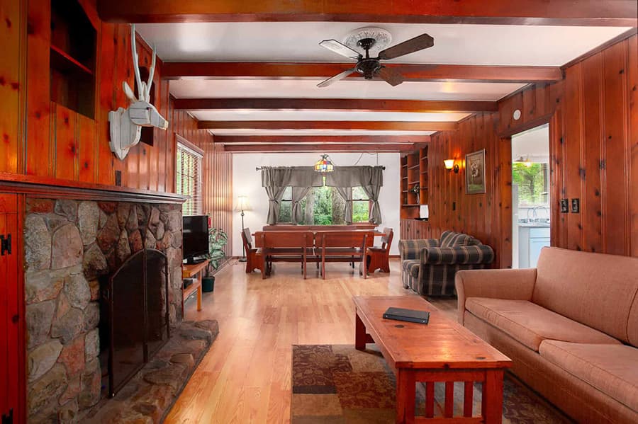 Cozy living room with wooden walls, a stone fireplace, and a mix of seating areas.
