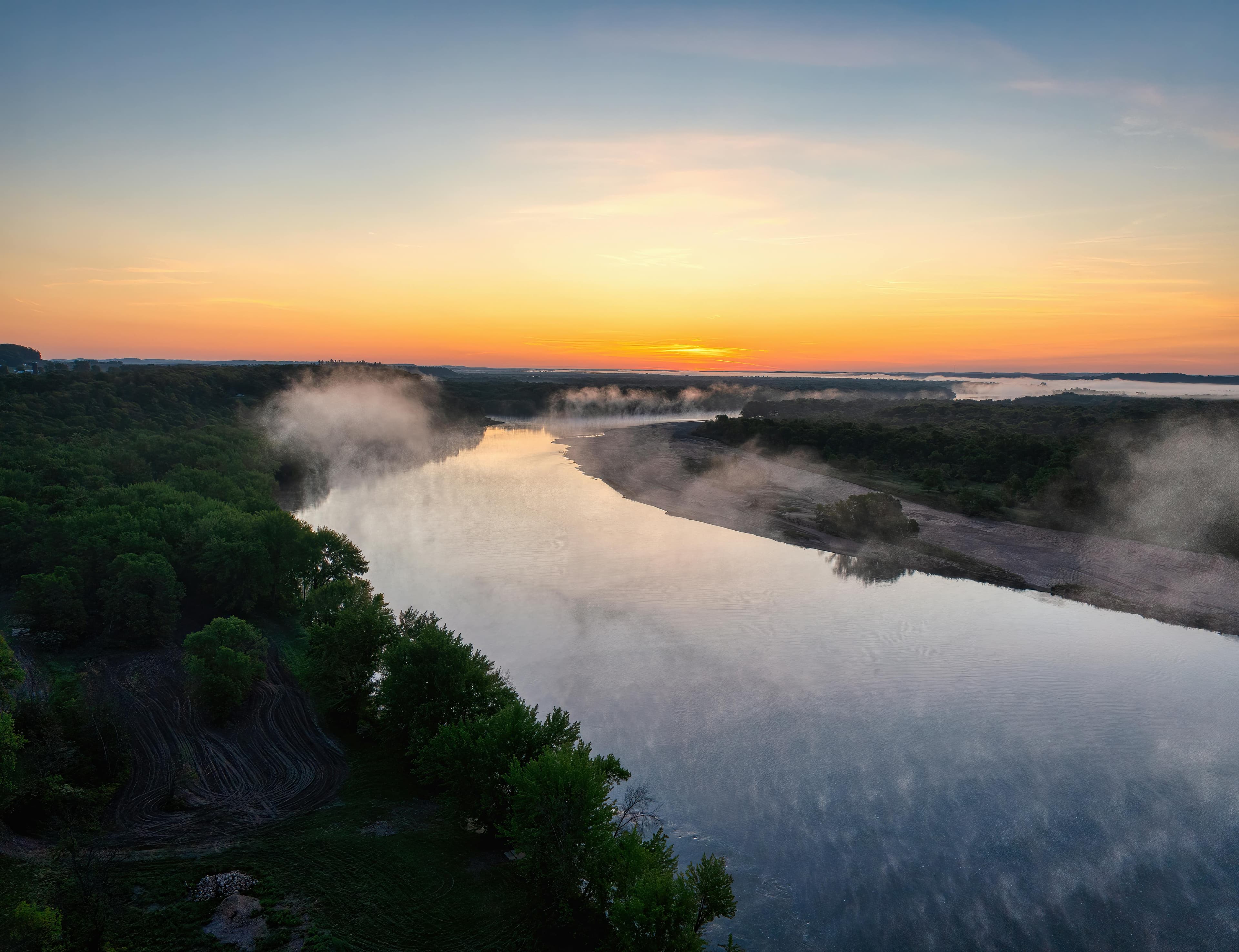 A serene river at sunrise, surrounded by mist and lush greenery.