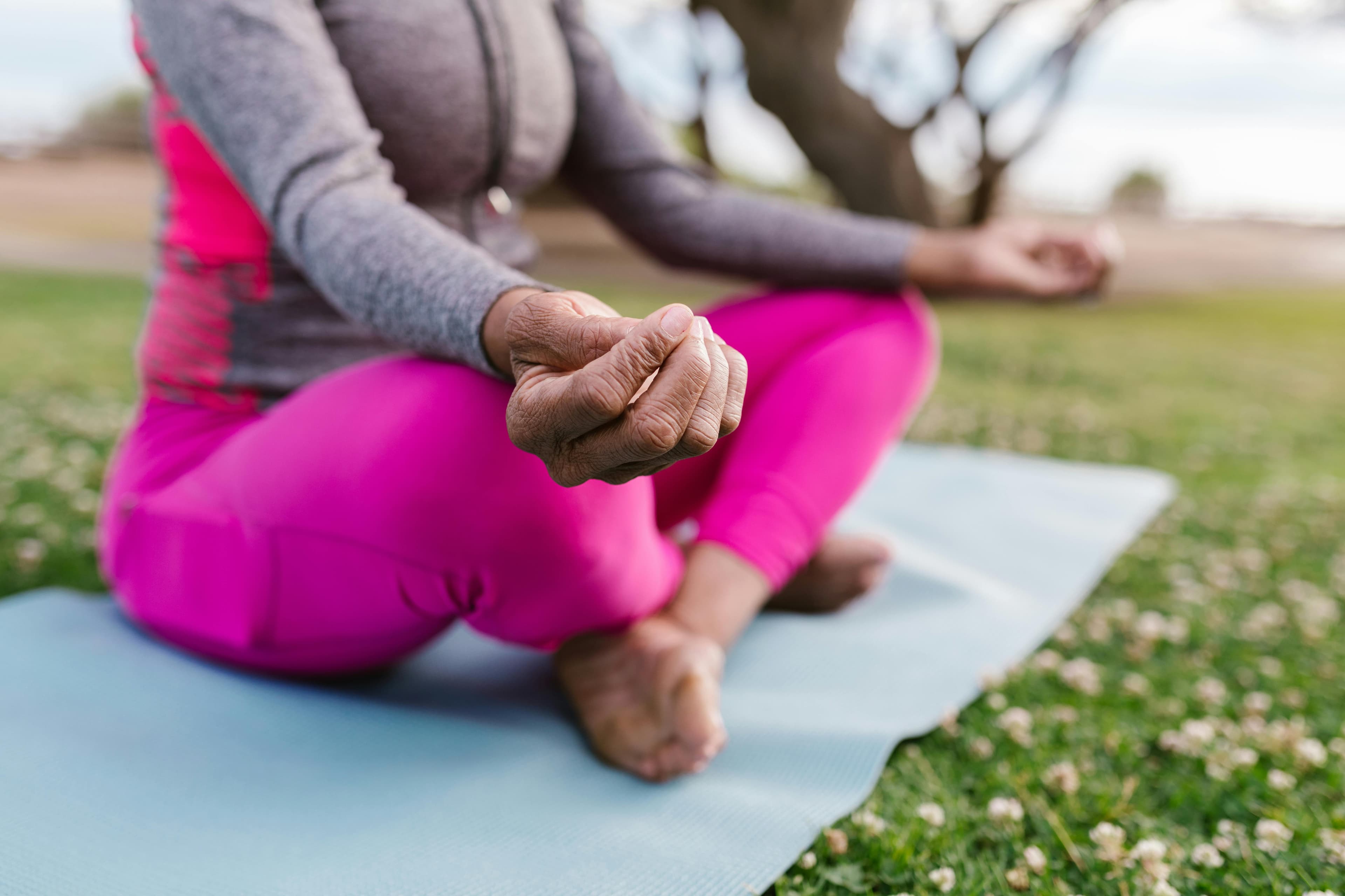 A person meditating in a seated position on a yoga mat in a grassy outdoor setting.