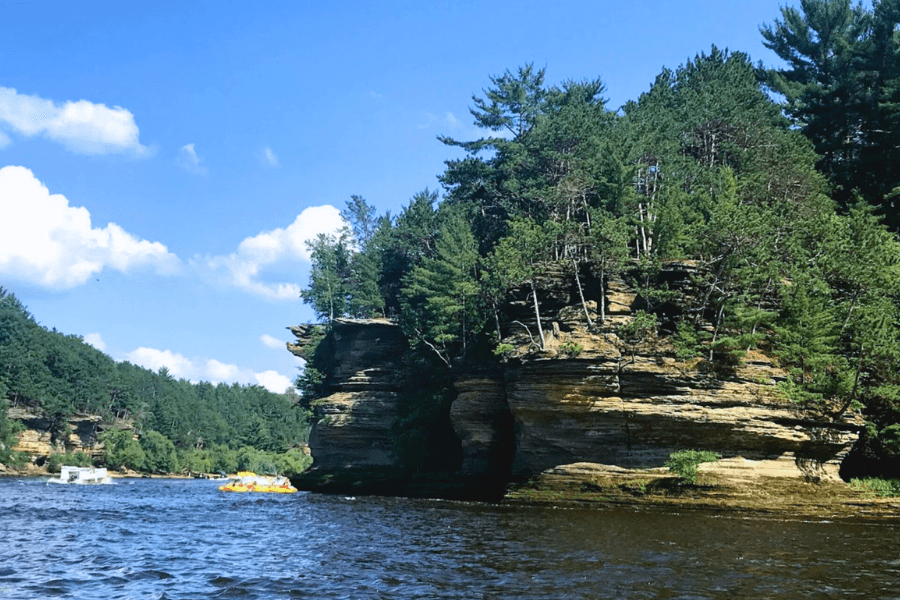 A rocky outcrop with dense trees rises above a river under a blue sky with fluffy clouds.