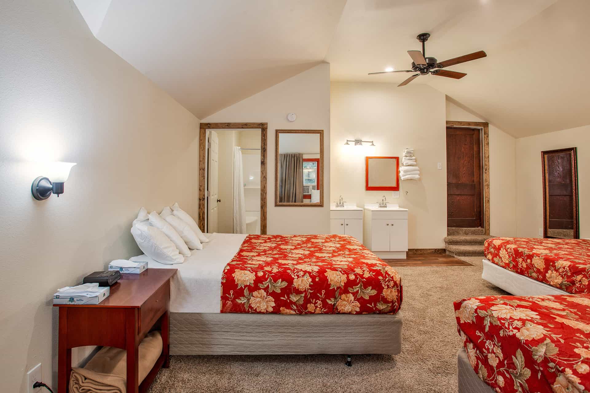 A brightly lit hotel room featuring two queen beds, a wooden nightstand, and a private bathroom.