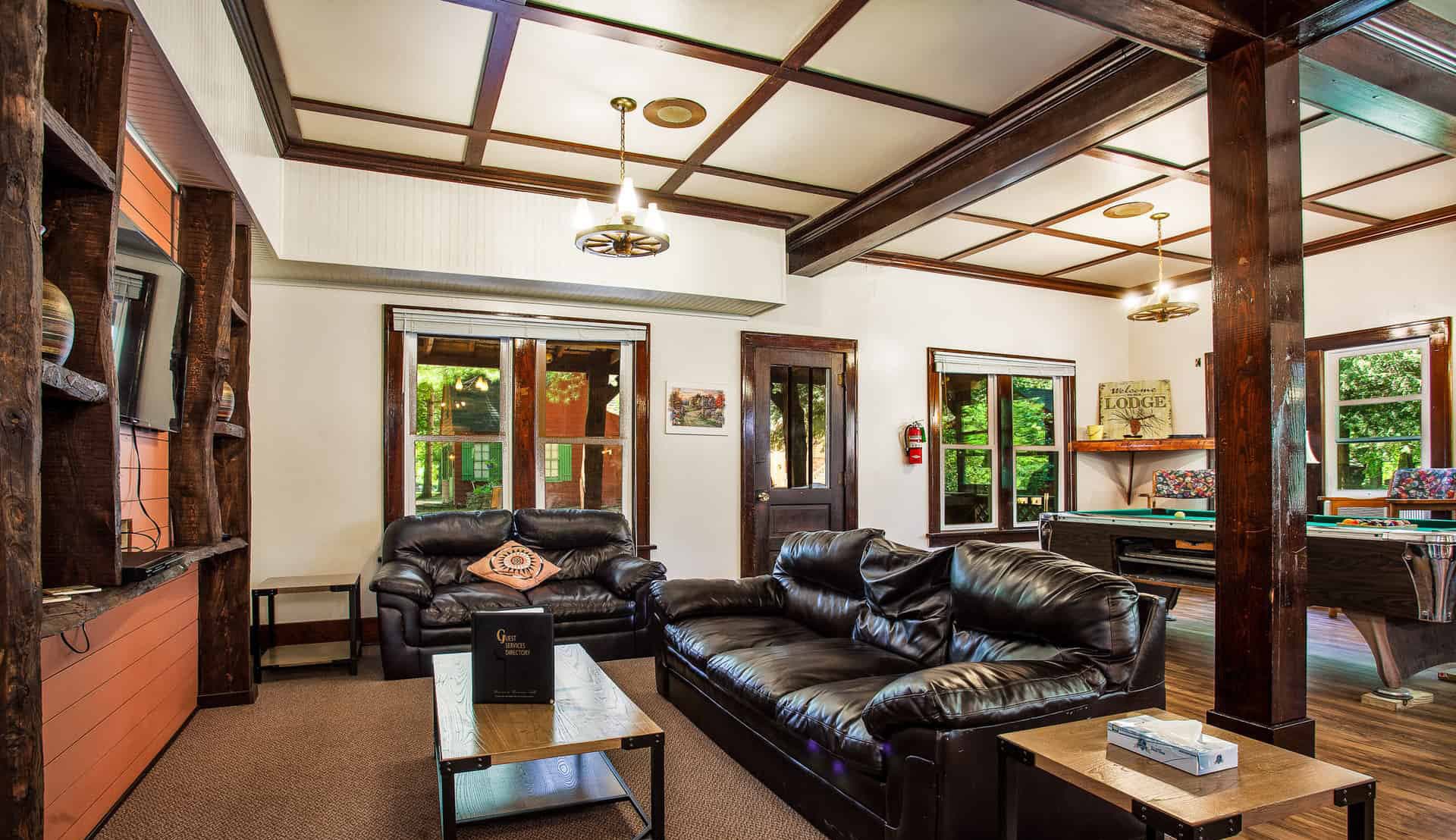 Cozy living room featuring black leather sofas, a wooden coffee table, and large windows.