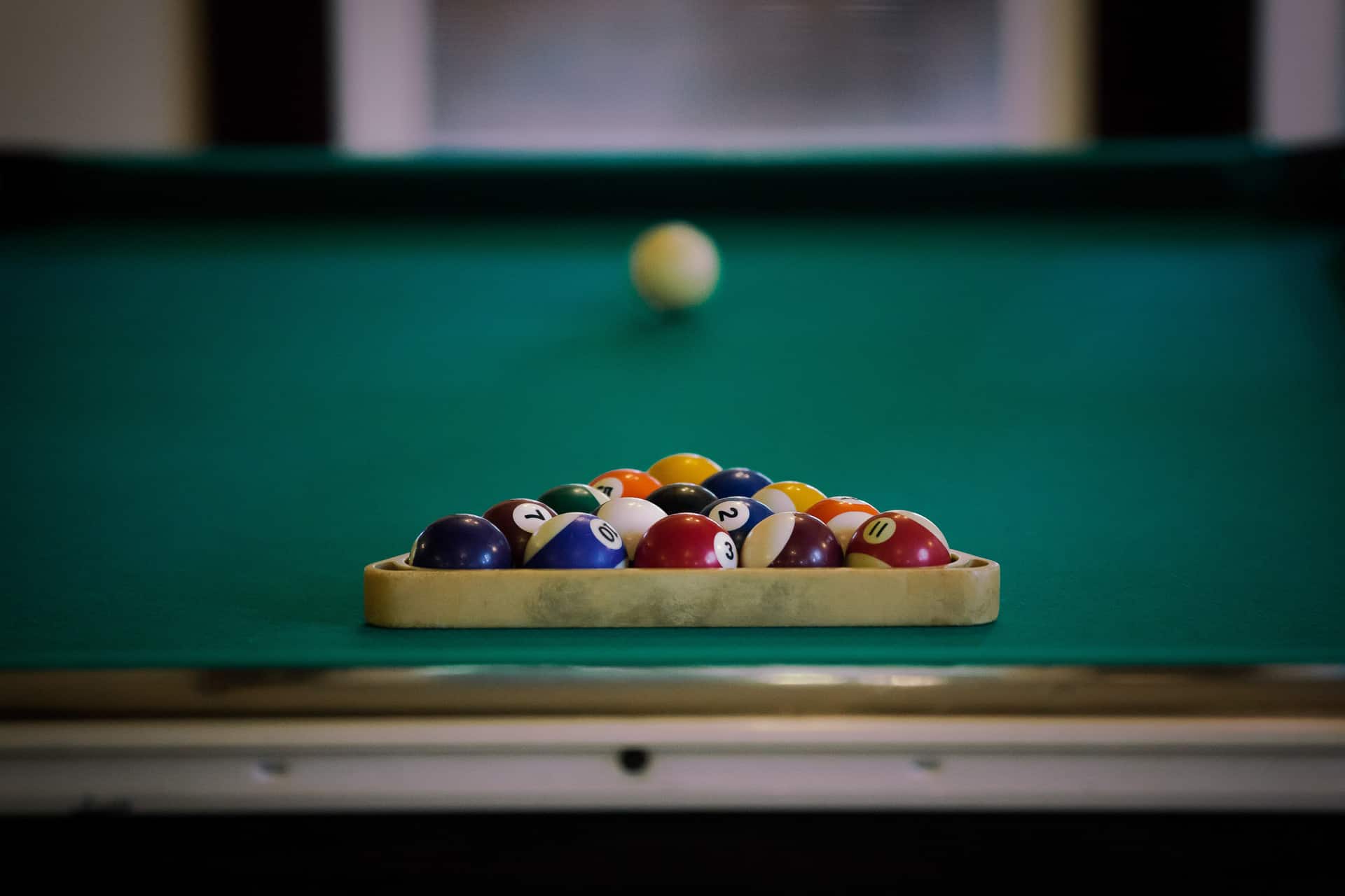A rack of billiard balls set up on a green pool table with a cue ball in the background.