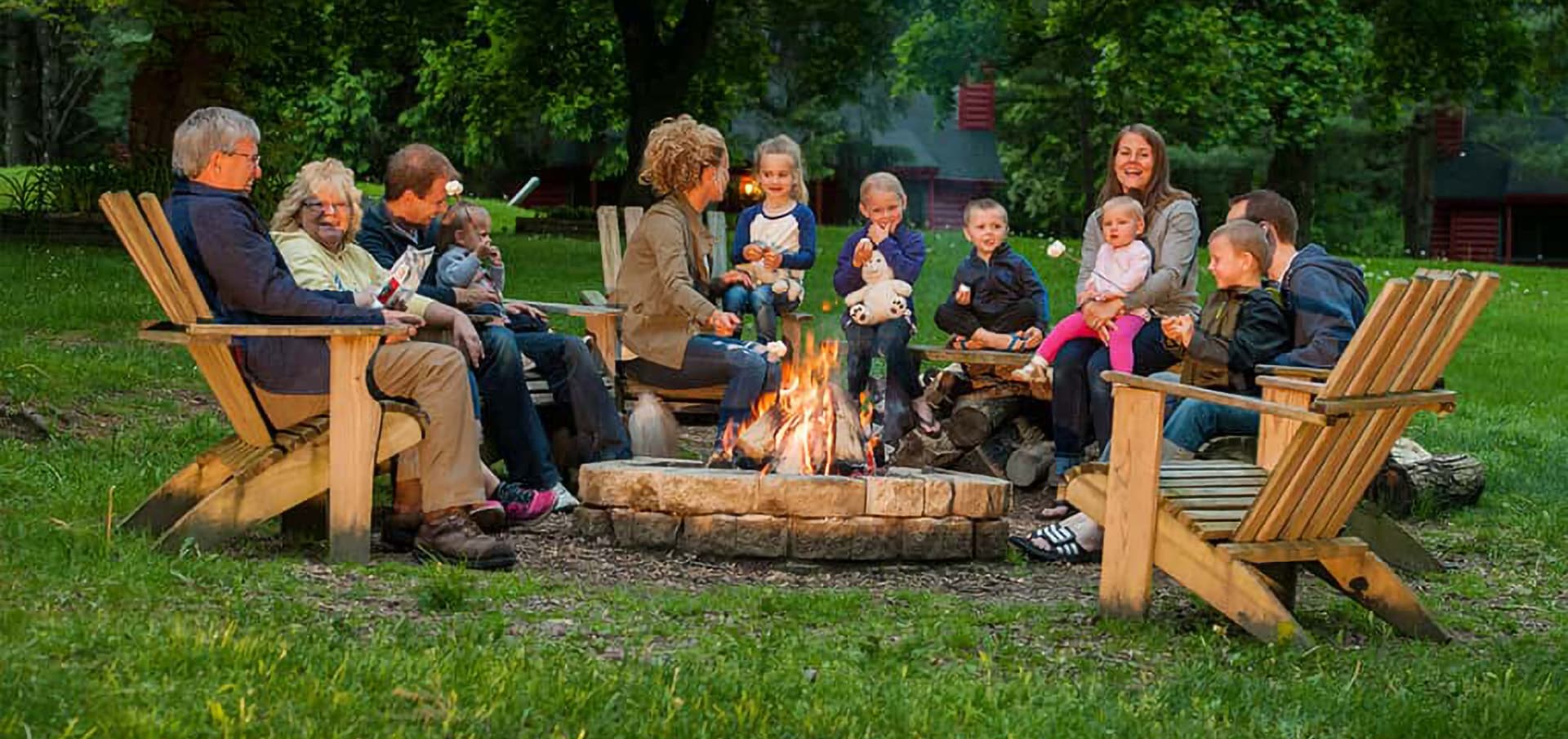 A group of family members sitting around a campfire in a grassy area, enjoying each other's company.