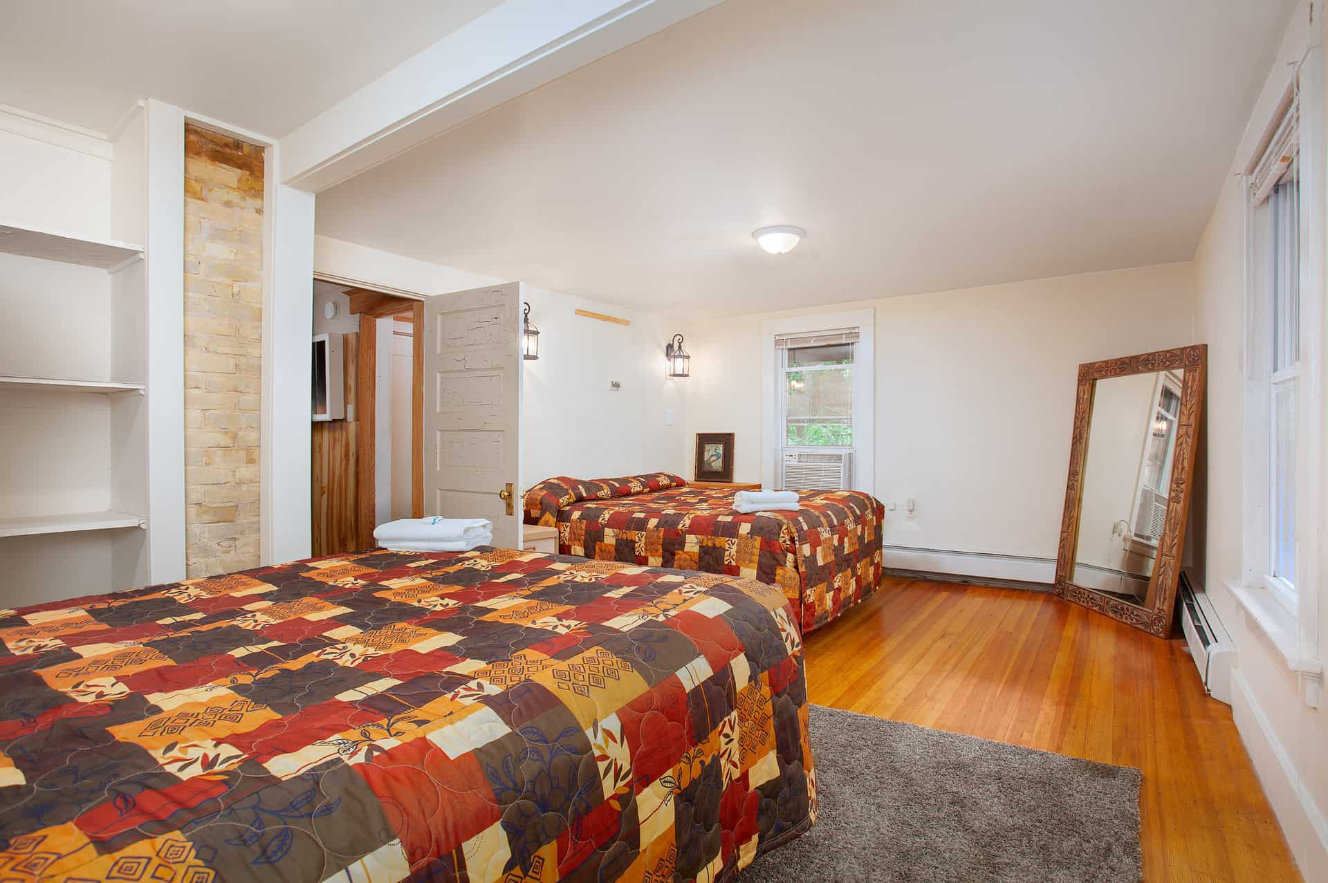 A cozy bedroom featuring two patterned beds, a mirror, and natural light.
