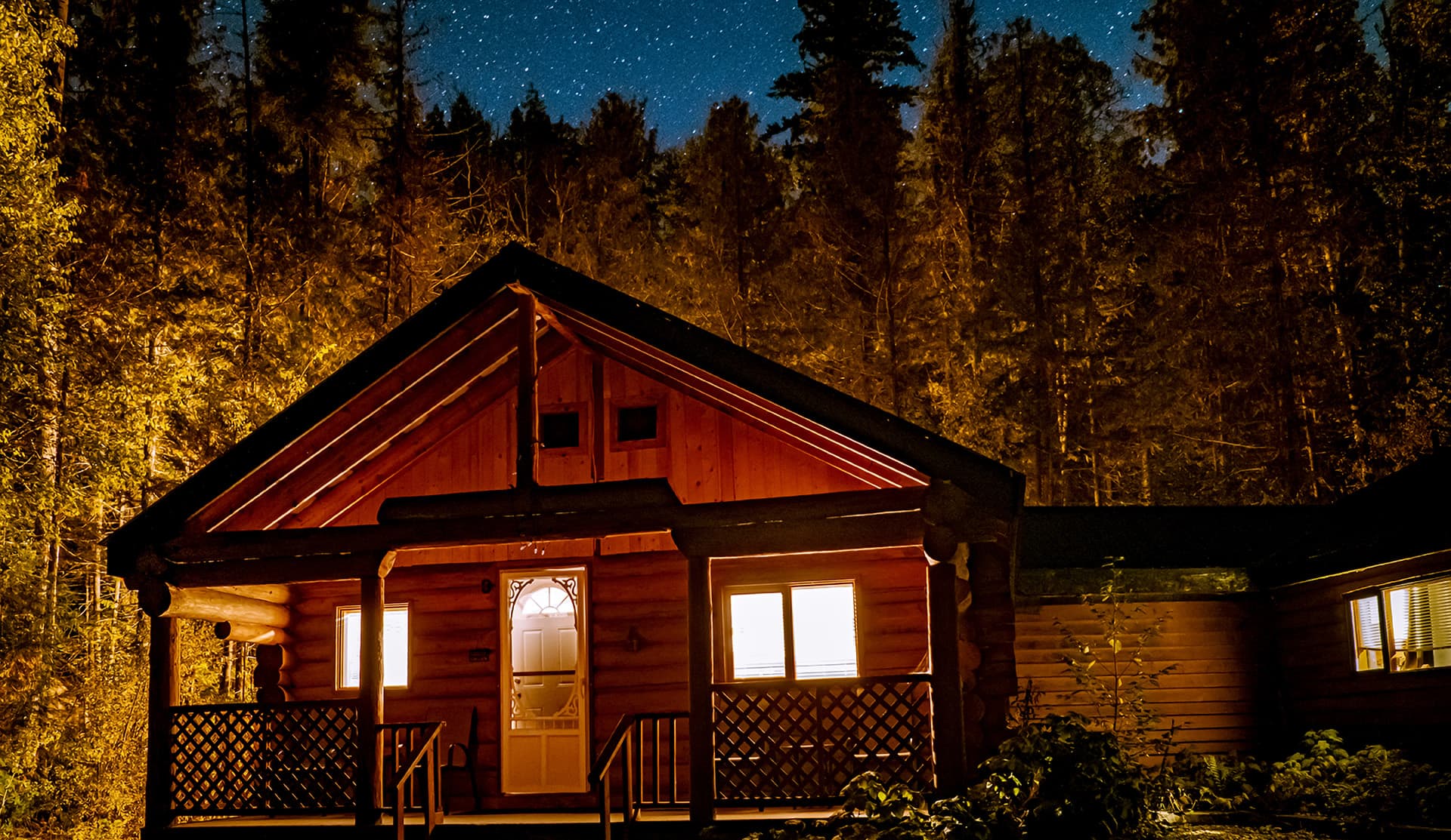 A log cabin surrounded by trees under a starry night sky.