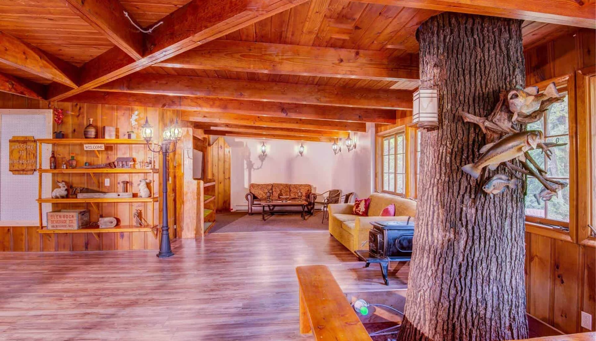 Cozy, rustic interior of a wooden cabin featuring a large tree post and comfortable seating.